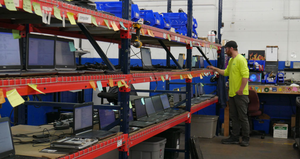 A worker looking at a rack full of refurbished laptop computers.